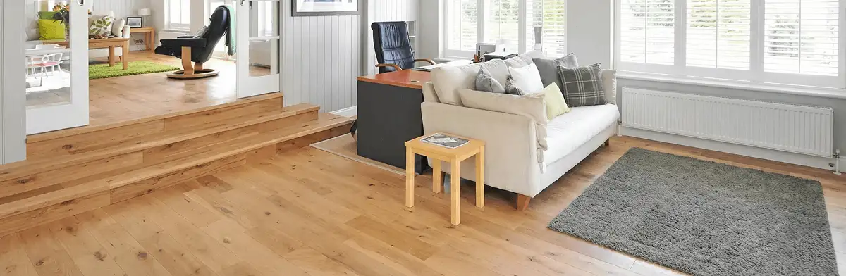 A modern living room with professionally installed laminate flooring, a beige sofa, a small side table, a gray rug, and large windows with white shutters in Cleveland, OH